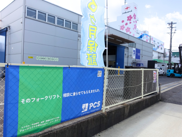 PCS名古屋営業所に掲げられた青と緑の横断幕。雲一つない青空の下に輝くフォークリフト相談用バナー。