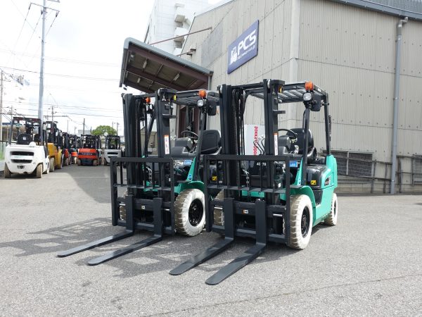 ピー・シー・エス千葉営業所に入庫した、三菱ロジスネクスト製2.5トンの新車ディーゼルフォークリフト（KFDE25P-T）が2台並んでいる様子